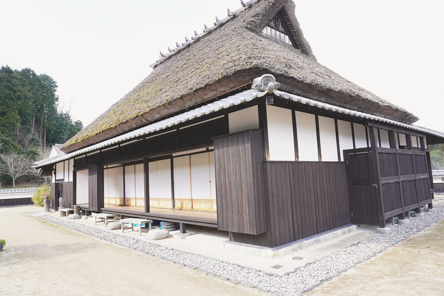砂利敷きの前庭ときれいに手入れされたかやぶきの家